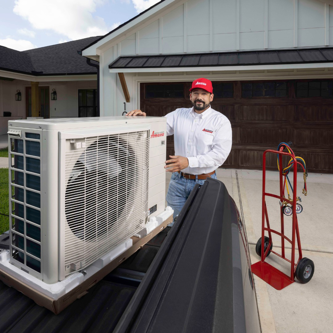 an amana ac installation tech next to a brand new AC unit smiling at the camera